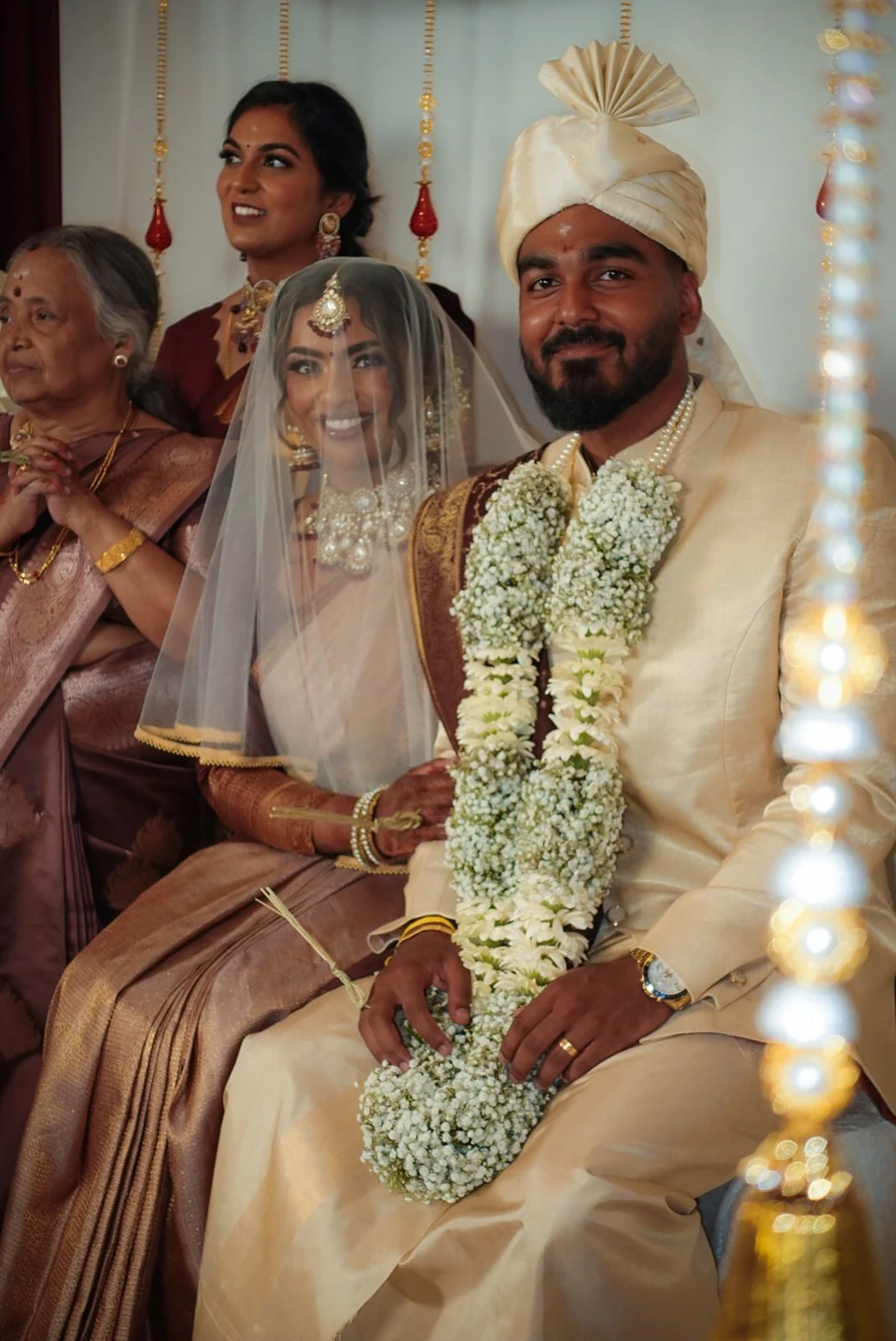 A seated wedding couple in ceremonial dress with family nearby